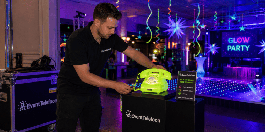 EventTelefoon medewerker plaatst een neon groene audiotelefoon op een glow in the dark feest, compleet met instructiebord en professionele installatie.