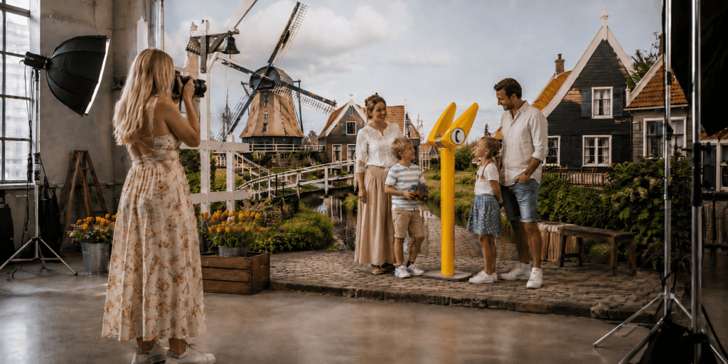 Fotografe maakt een familiefoto bij een gele ANWB-praatpaal in een Nederlands decor met molens, houten huizen en tulpen.