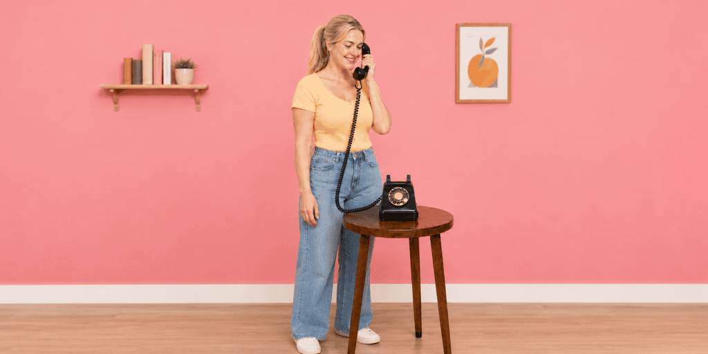**Alt-tekst:**
Vrouw luistert via een zwarte retro telefoon naar de welkomstboodschap van het audiogastenboek.
