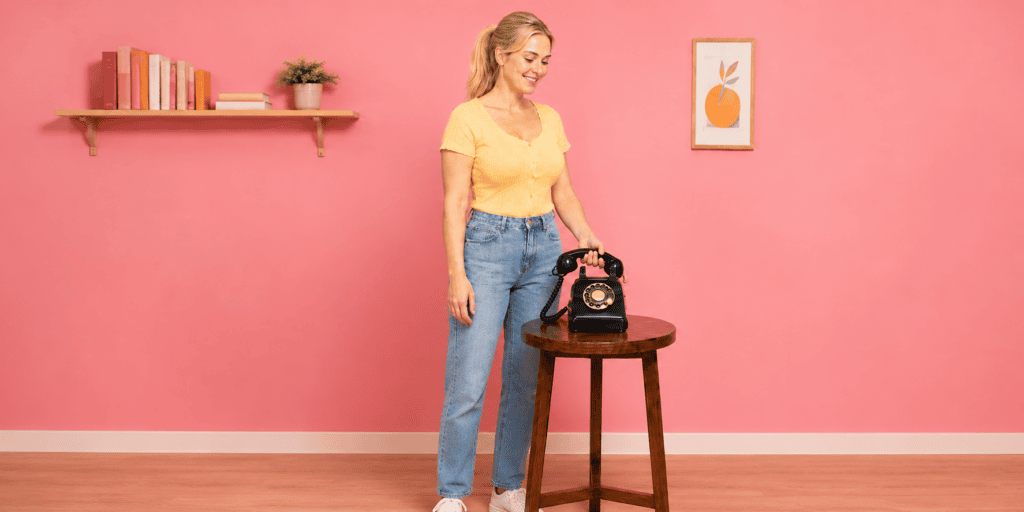 **Alt-tekst:**
Vrouw luistert via een zwarte retro telefoon naar de welkomstboodschap van het audiogastenboek.
