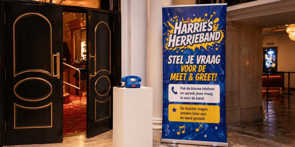 Blauwe EventTelefoon op een witte zuil naast een banner van Harrie’s Herrieband, waar fans vragen inspreken voor de meet & greet.