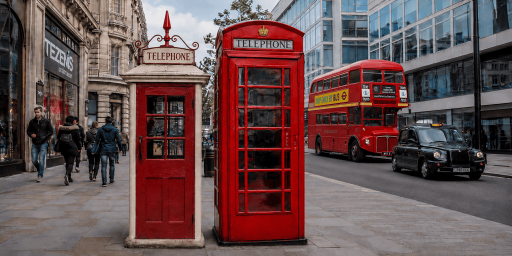 Historische rode telefooncel en Britse K6-telefooncel in een Londense winkelstraat, met rode dubbeldekker en zwarte taxi op de achtergrond.