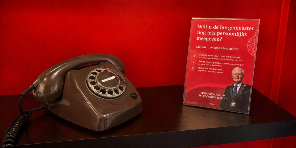 Mocca bruine retro draaischijftelefoon van Eventtelefoon op een zwarte plank tegen een rode achtergrond