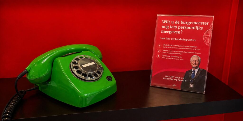 Groene retro draaischijftelefoon van Eventtelefoon op een zwarte plank tegen een rode achtergrond