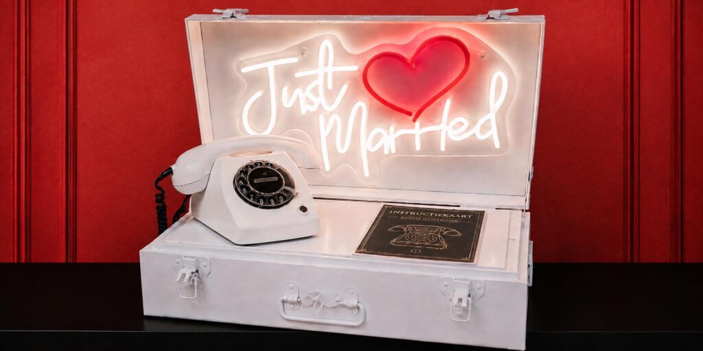 Witte retro draaischijftelefoon van eventtelefoon in een open witte neonbox koffer met verlicht neonbord “Just Married”