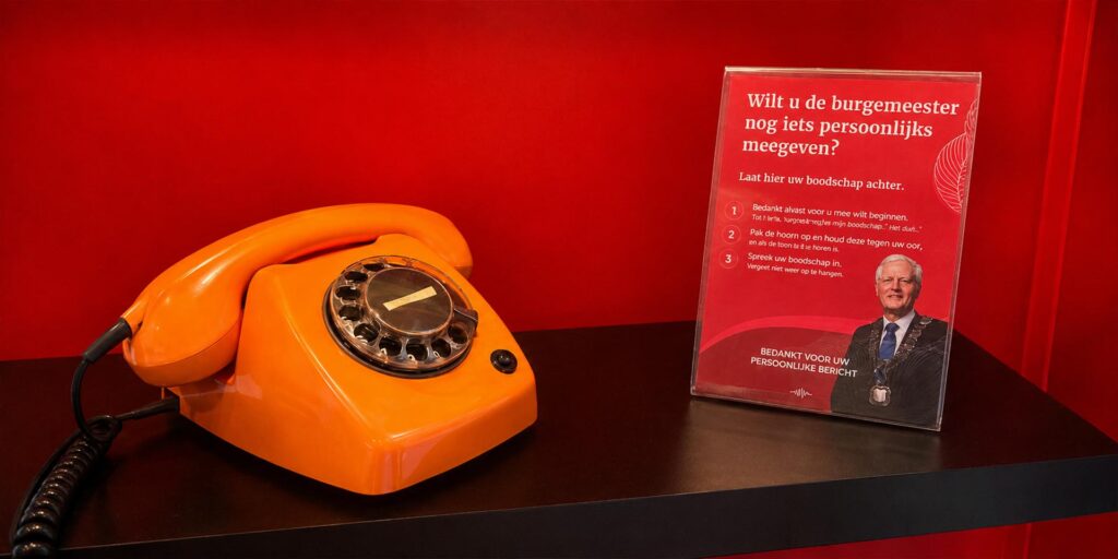 Oranje retro draaischijftelefoon van Eventtelefoon op een zwarte plank tegen een rode achtergrond