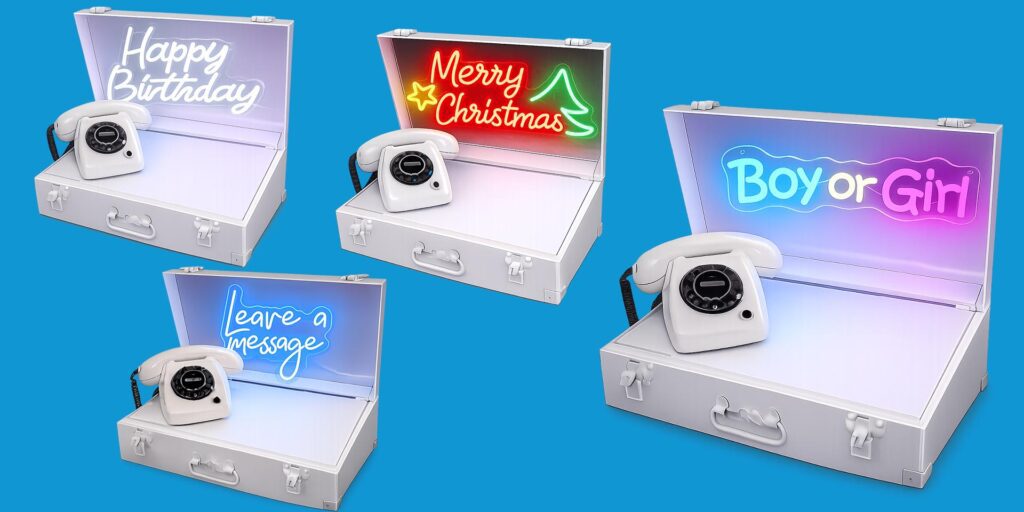 Vier witte neonboxen van eventtelefoons in open koffers met verlichte neonborden voor verschillende gelegenheden, waaronder ‘Happy Birthday’, ‘Merry Christmas’, ‘Leave a message’ en ‘Boy or Girl’.