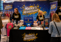 Merchandisestand van Harrie’s Herrieband met fans, medewerkers en een blauwe EventTelefoon waarmee bezoekers vragen inspreken voor de meet & greet.